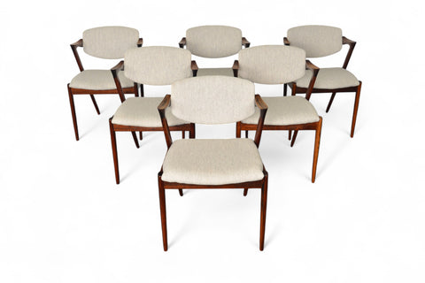 A set of six Kai Kristiansen model 42 dining chairs made of rosewood, with beige upholstered seats, arranged around a circular dining table.