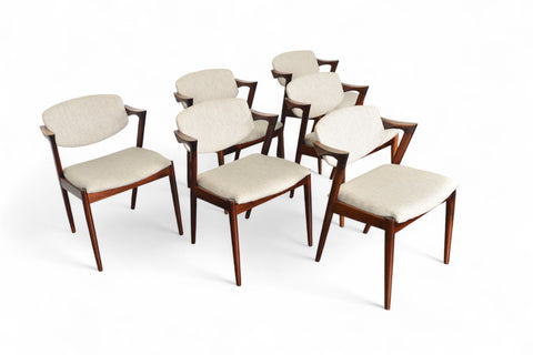 A set of six Kai Kristiansen model 42 dining chairs made of rosewood, with beige upholstered seats, arranged around a circular dining table.