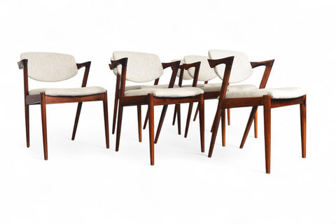 Set of six wooden chairs with white cushions on a white background