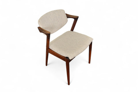 A set of six Kai Kristiansen model 42 dining chairs made of rosewood, with beige upholstered seats, arranged around a circular dining table.