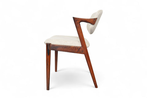 A set of six Kai Kristiansen model 42 dining chairs made of rosewood, with beige upholstered seats, arranged around a circular dining table.