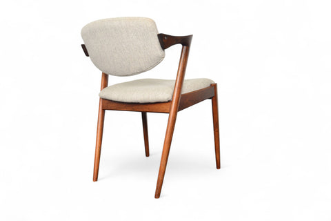 A set of six Kai Kristiansen model 42 dining chairs made of rosewood, with beige upholstered seats, arranged around a circular dining table.