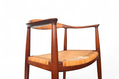 A Hans Wegner JH-501 round chair with teak wood frame and cane seating, displayed against a white background.