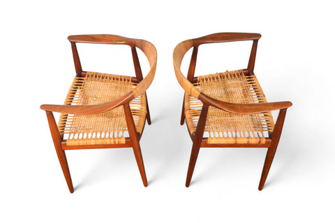 A pair of Hans Wegner JH-501 round chairs with teak wood frames and cane seating, displayed against a white background.