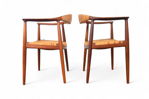A pair of Hans Wegner JH-501 round chairs with teak wood frames and cane seating, displayed against a white background.