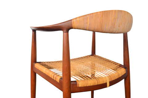 A Hans Wegner JH-501 round chair with teak wood frame and cane seating, displayed against a white background.