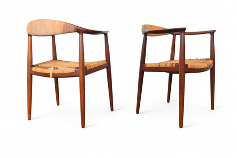 A pair of Hans Wegner JH-501 round chairs with teak wood frames and cane seating, displayed against a white background.
