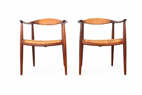 A pair of Hans Wegner JH-501 round chairs with teak wood frames and cane seating, displayed against a white background.