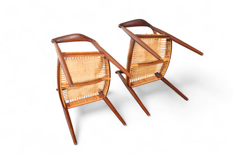 A pair of Hans Wegner JH-501 round chairs lying on their sides with teak wood frames and cane seating, displayed against a white background.