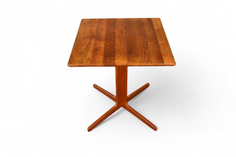 A small solid teak wood mid-century pedestal base dining table with a visible drawer and a smooth finish.